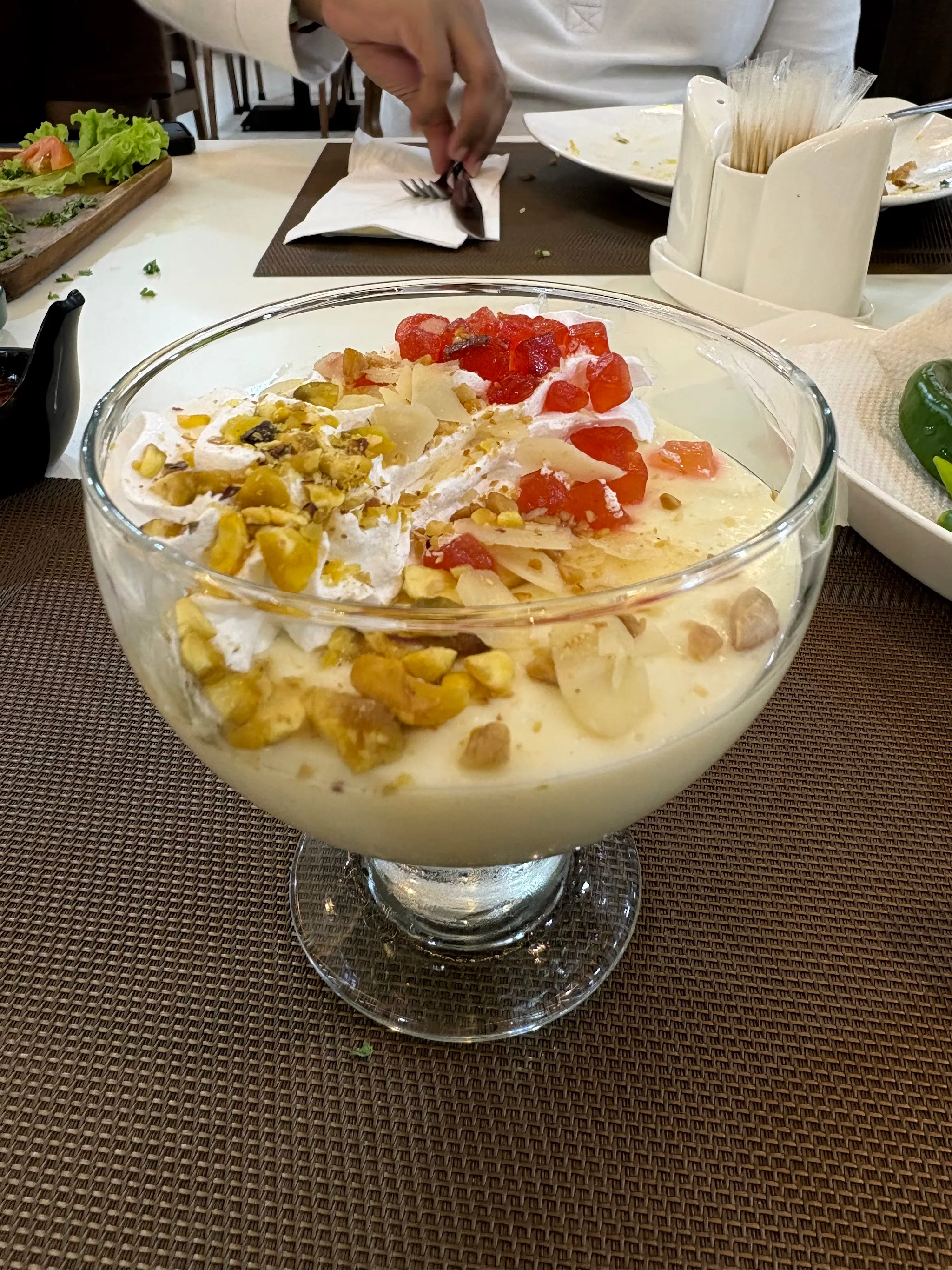 Bowl of cream dessert topped with pistachios, nuts and candied fruit