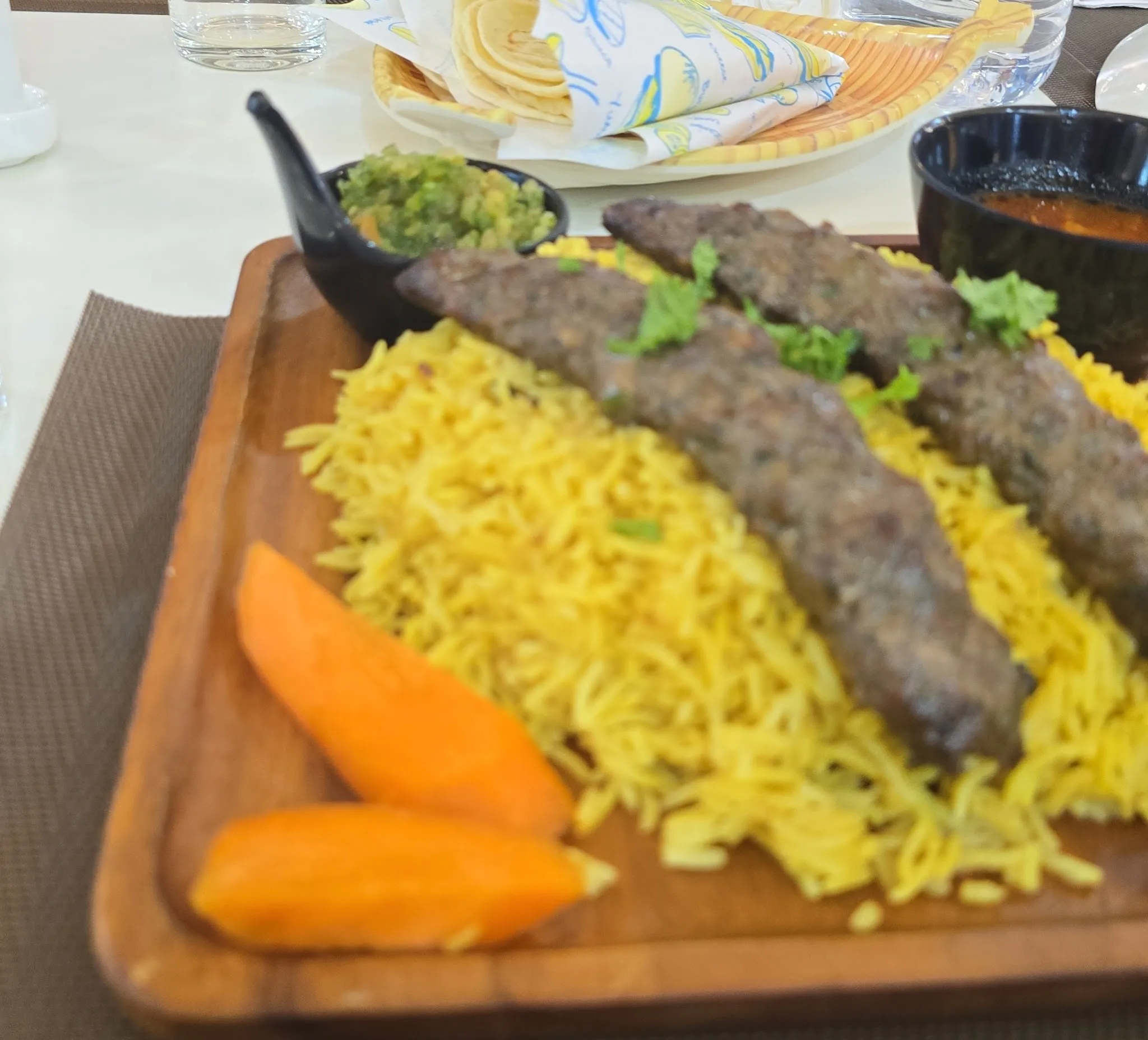 Kofta kebab served over turmeric rice with grilled carrot and green salsa